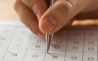 Fotografia colorida ilustra a matéria "OAB aprova livre escolha de local e inclui 3 disciplinas no Exame de Ordem". Na imagem vemos a mão de uma pessoa simulando o preenchimento do gabarito do exame da Ordem.