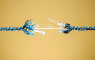 Ilustrando a capa da matéria “Como evitar o Burnout na advocacia”, temos a foto de uma corda quase rompida ao meio, apenas um fio impede o corte total.