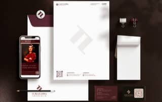 Como capa da matéria “Identidade visual para escritórios de advocacia”, vemos itens de papelaria com o logotipo da Flávia Lopes e um celular exibindo a página principal do site como exemplos de identidade visual.