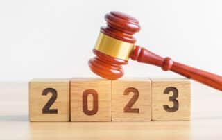 Como capa da matéria “7 Tendências do Direito para 2023”, vemos um martelo de juiz sobre uma mesa e quatro blocos com números representando o ano de 2023.