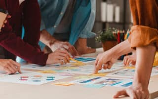 Como capa da matéria “Como usar metodologias ágeis na advocacia”, vemos um grupo de pessoas em uma mesa cheia de papéis e post-its debatendo sobre um projeto.