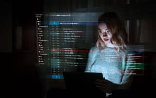 Como capa da matéria “ChatGPT na Advocacia: Inteligência Artificial no mbito Jurídico”, vemos uma mulher trabalhando com programação, onde uma tela com códigos flutua na frente dela.