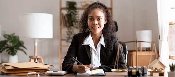 Advogada sentada em uma mesa de escritório fazendo anotações. Advogada sentada em uma mesa de escritório fazendo anotações.