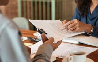 Como capa da matéria “Estratégias para Negociação de Contratos na Advocacia”, vemos uma advogada entregando um contrato para um cliente.